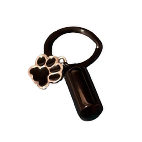 A black cylindrical pendant, designed as a pet cremation urn charm, hangs from a ring next to a silver-colored paw print charm.