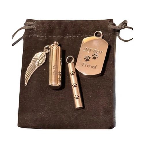 Three silver pet remembrance charms, including a dog tag reading "MY best Friend" and two small cylindrical cremation pendants, are arranged on a black velvet bag.